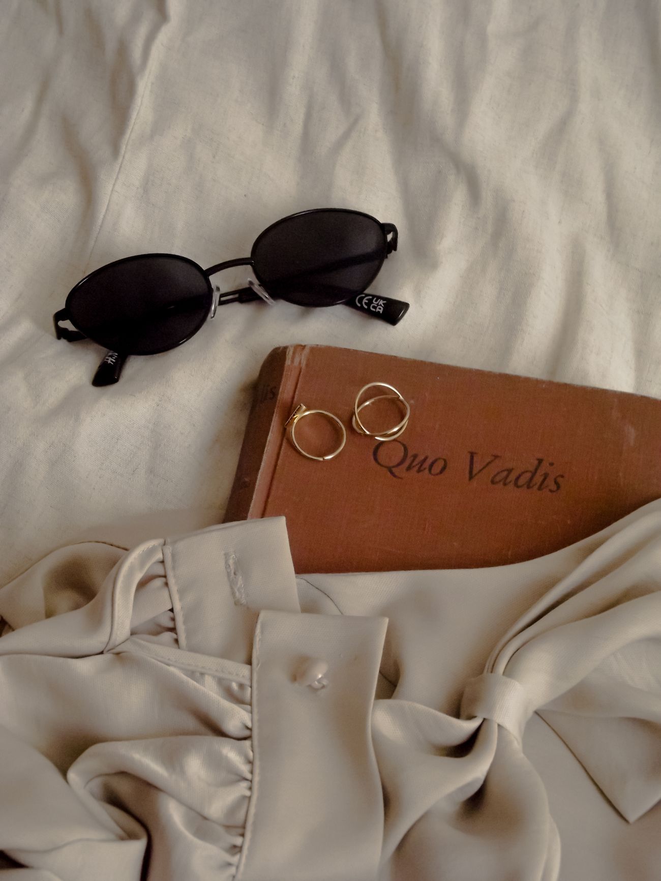 A warm flat-lay of everyday style — sunglasses, rings, a good book